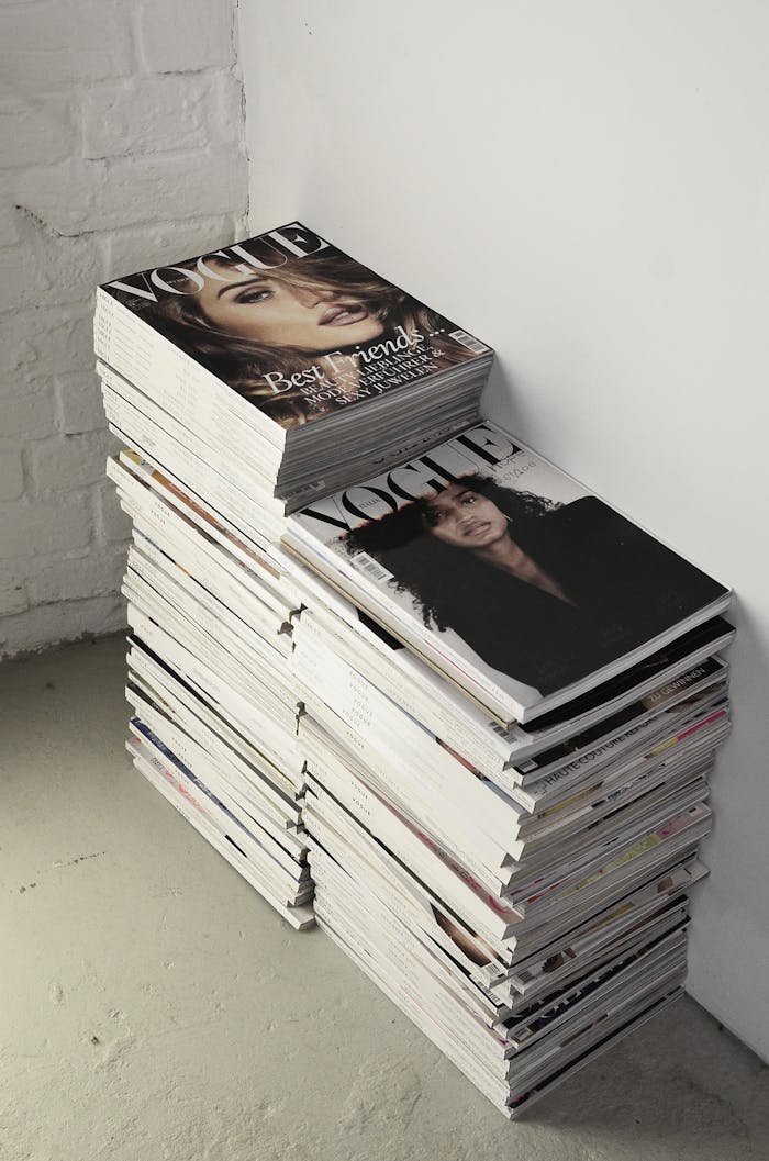 High angle many fashion magazines stacked on floor against white brick wall in studio